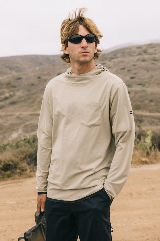 Wearing black sunglasses and the 686 Mens Lets Go Tech Hoody, a person stands outdoors on a dirt path with dry, hilly terrain in the background.