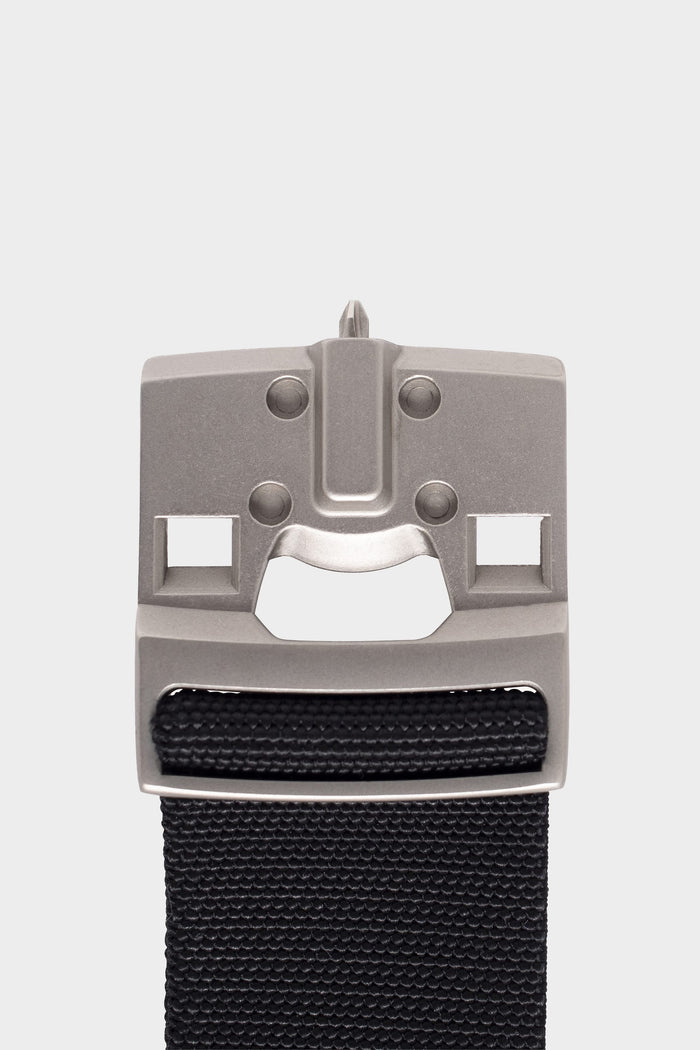 A close-up of the 686 Westwell Clicker Stretch Belt by 686, featuring a metallic buckle with a stylized face design on a black fabric strap, set against a plain white background.