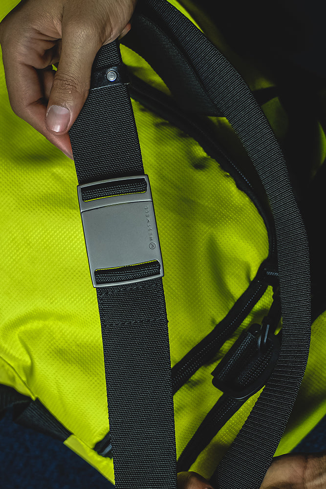 A hand holds the 686 Westwell Clicker Stretch Belt by 686, featuring a silver buckle, placed on a bright yellow textured surface.