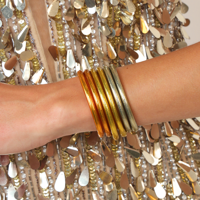 Golden Core Mixed Stack featuring a collection of radiant bangles on a wrist against a backdrop of shimmering fabric.