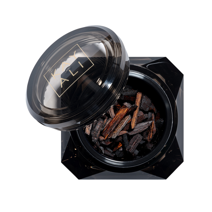Black container with lid featuring a brand logo, filled with dark brown sticks on a white background.