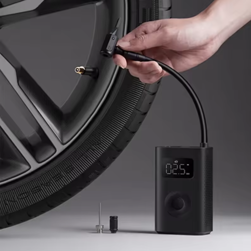 Hand using a digital tire inflator on a car tire with a gray background