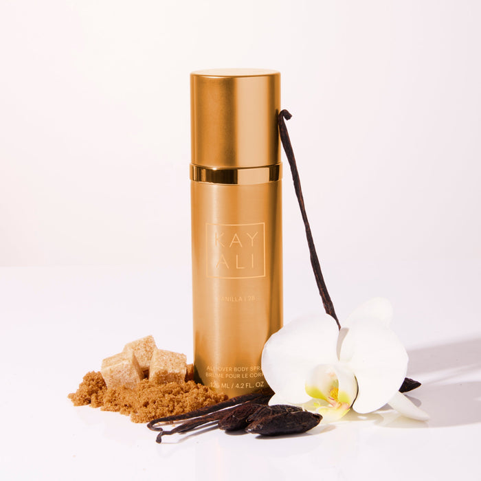 Gold bottle labeled 'KAYALI' with vanilla beans, sugar, and an orchid on a white background
